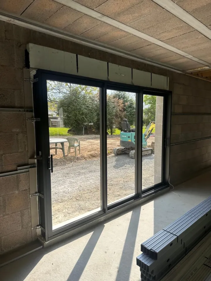 Baie coulissante gris foncé posée dans une ouverture en maçonnerie, chantier en cours