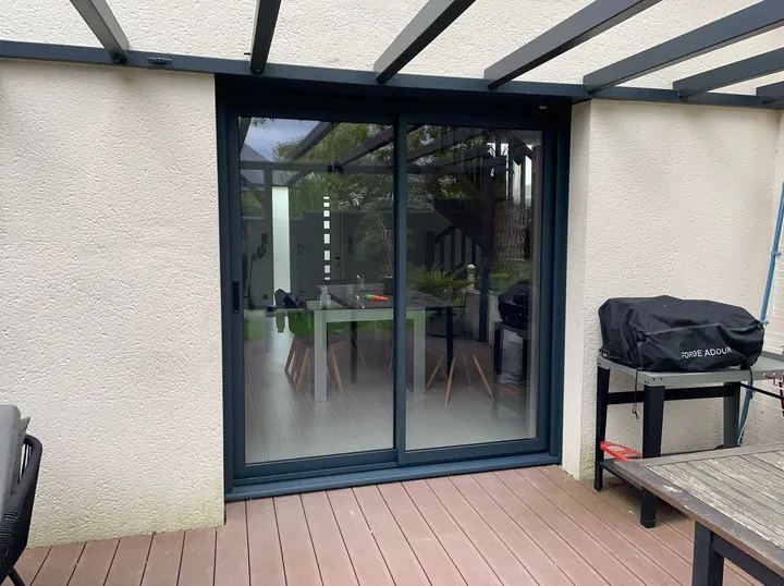 Baie coulissante anthracite donnant sur une terrasse en bois sous une pergola
