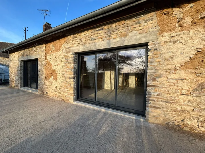 Grandes baies anthracite intégrées à une façade en pierre avec terrasse