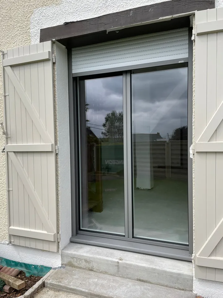Fenêtre grise avec volets battants blancs ouverts dans une façade enduite