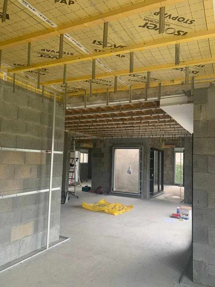 Isolant jaune et rails métalliques au plafond d’une pièce en maçonnerie