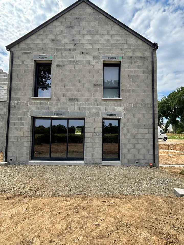 Menuiseries sombres réparties sur les deux niveaux d’un pignon en maçonnerie, chantier en cours