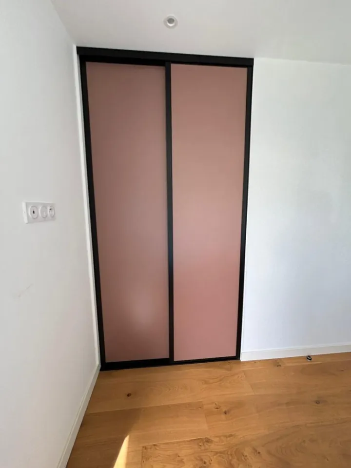 Placard avec façades coulissantes roses et cadres noirs dans une chambre