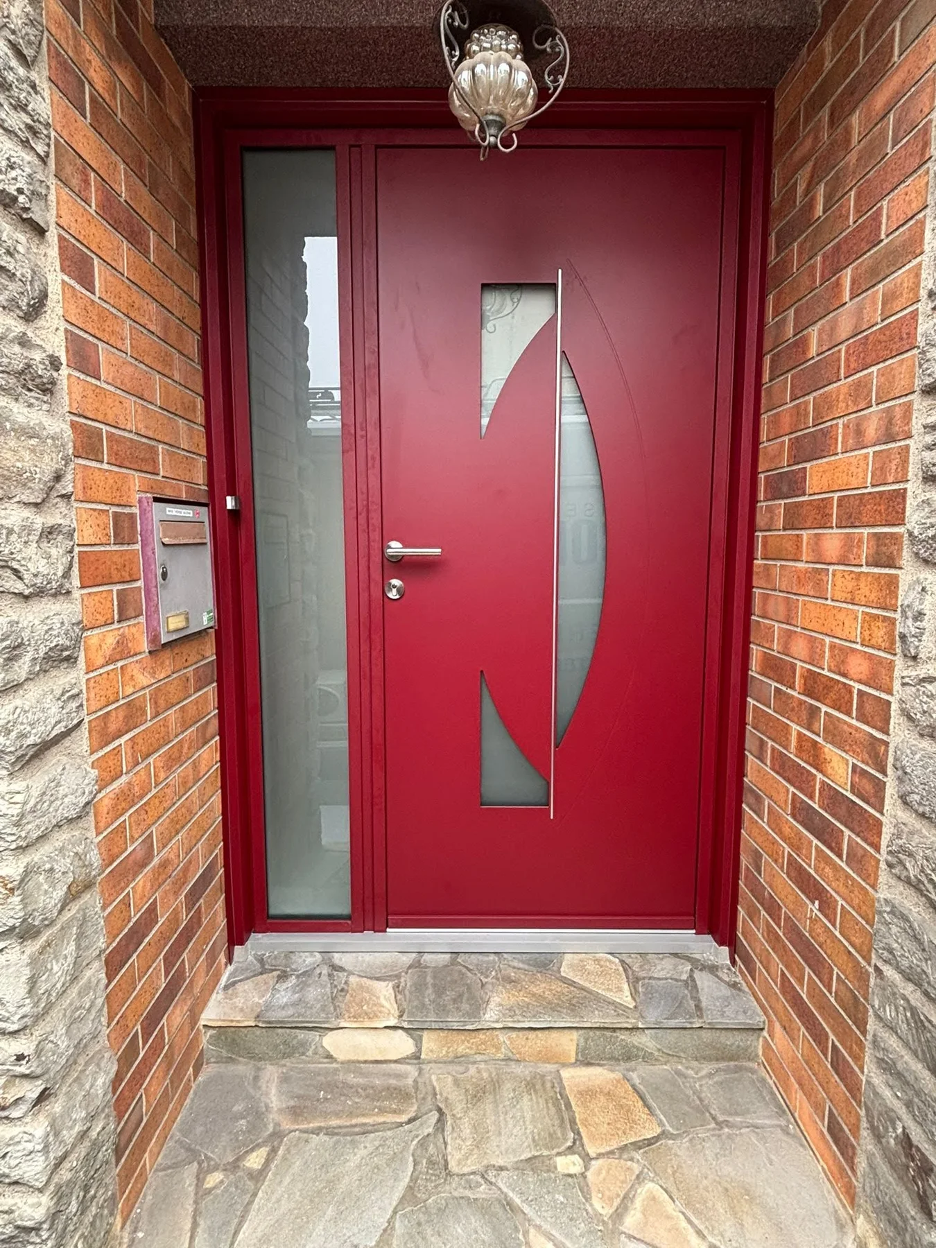 Porte d’entrée rouge avec vitrage décoratif, dans un encadrement en brique