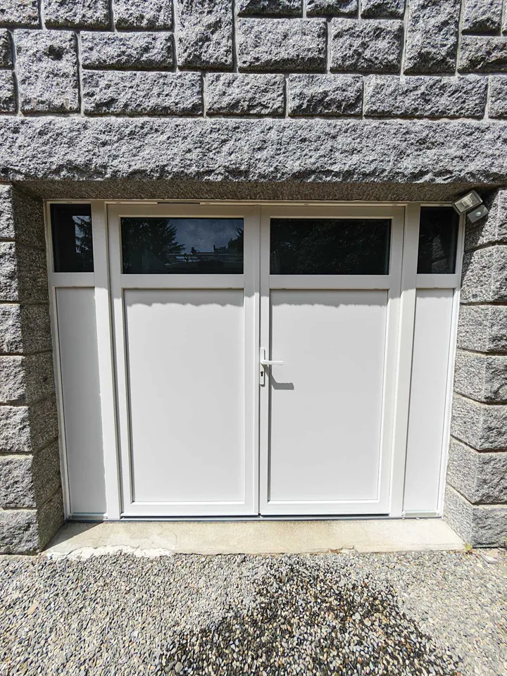 Porte de garage claire avec vitrages hauts dans une façade en pierre