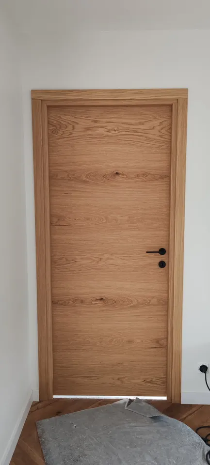 Porte intérieure pleine aspect bois avec poignée noire, finitions du chantier en cours