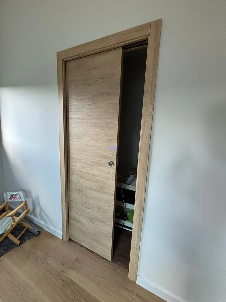 Porte intérieure coulissante aspect bois entrouverte dans une cloison