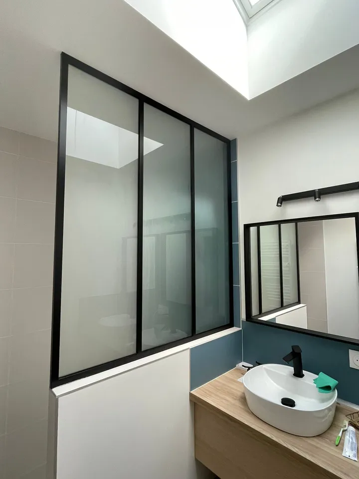 Verrière noire au-dessus d’un meuble vasque dans une salle d’eau