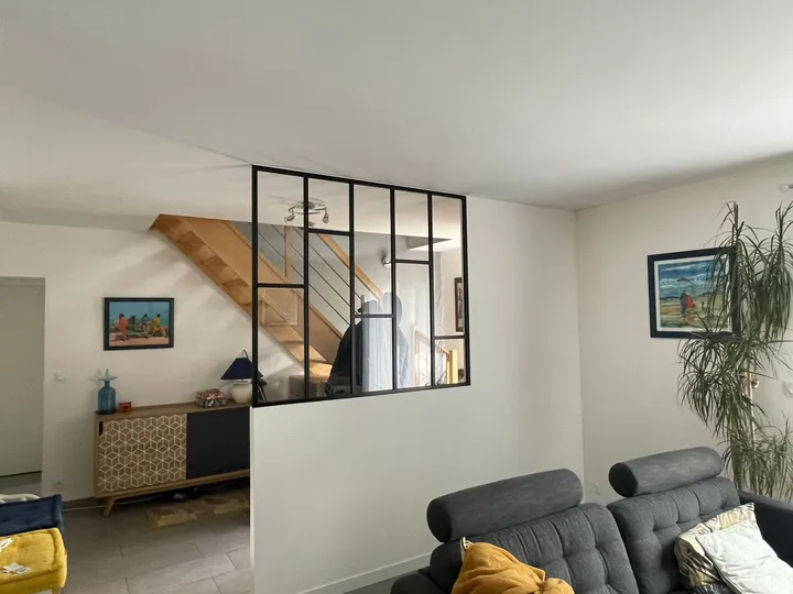 Verrière noire sur une cloison basse entre un séjour et un escalier