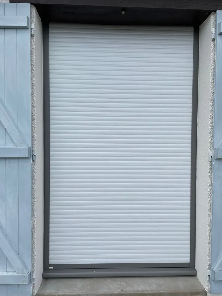 Volet roulant blanc fermé devant une fenêtre en façade