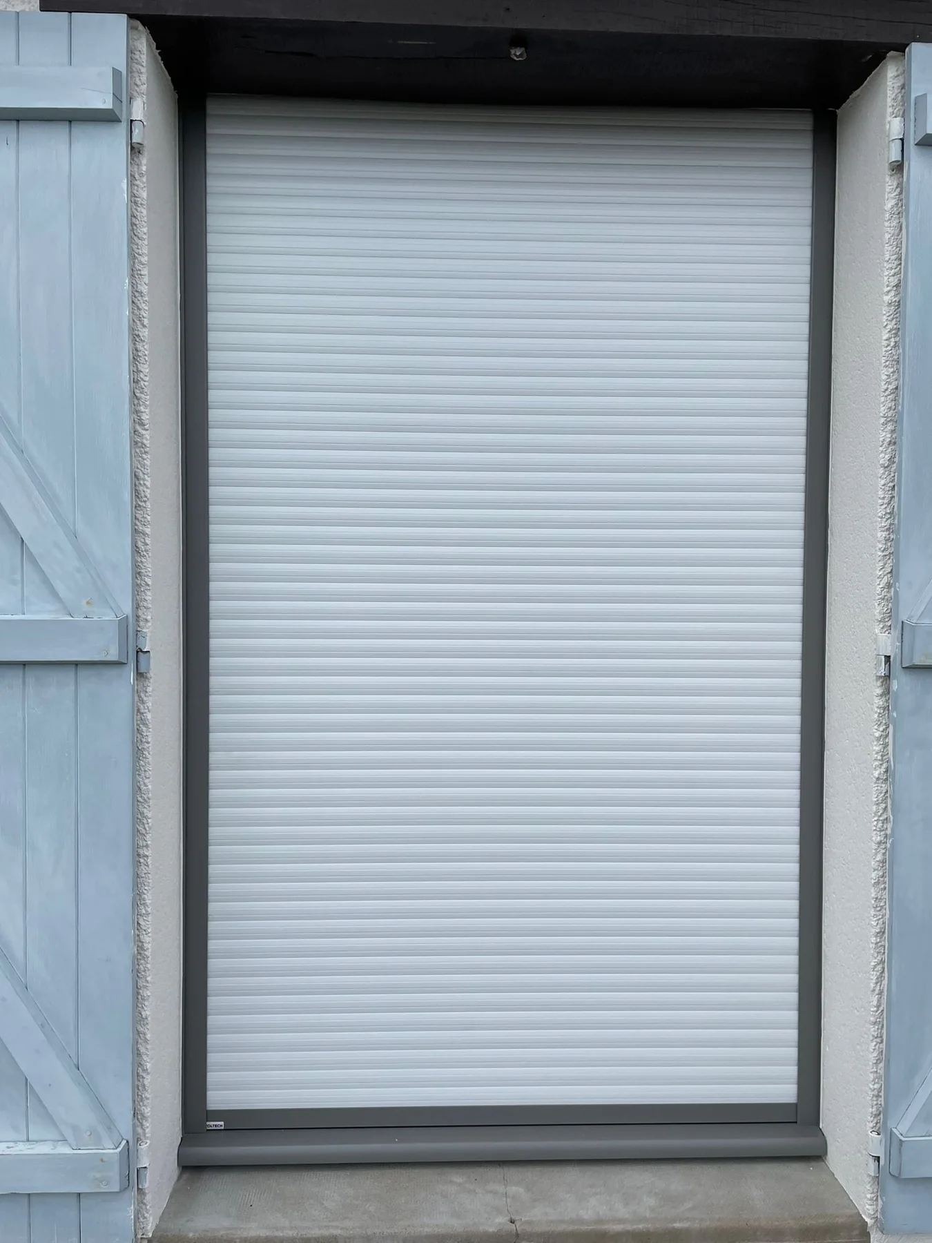 Volet roulant blanc fermé devant une fenêtre en façade